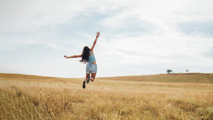 woman jumping for joy in open field and arms raised