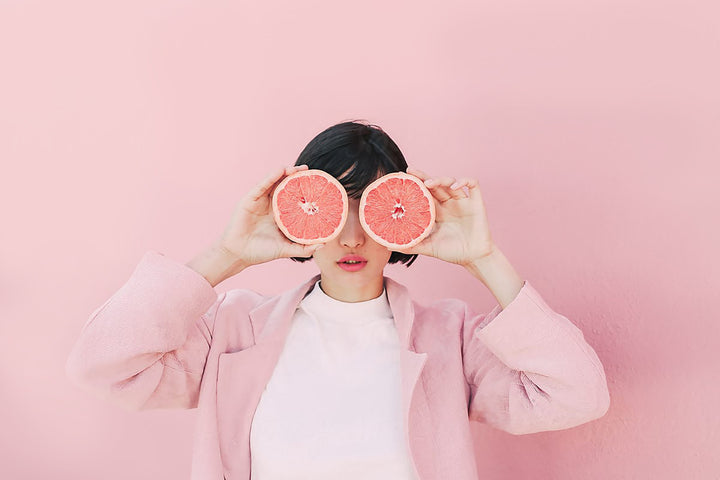 Woman in Front of Pink Background Holding Grapefruits