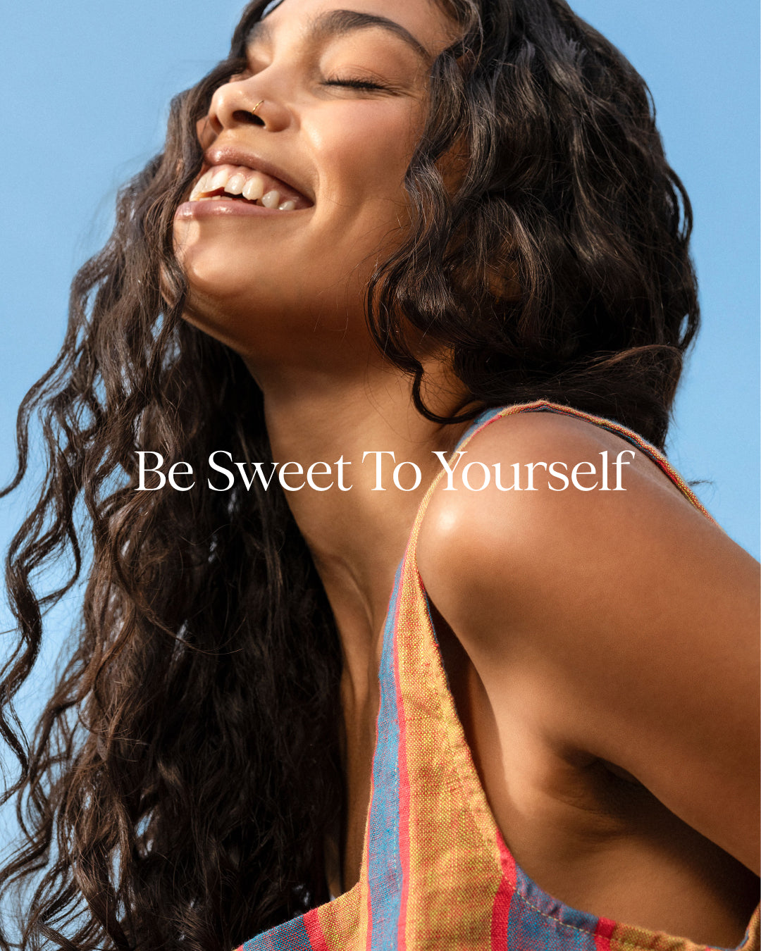 Woman with a bright smile against a clear blue sky with 'Be Sweet To Yourself' text.