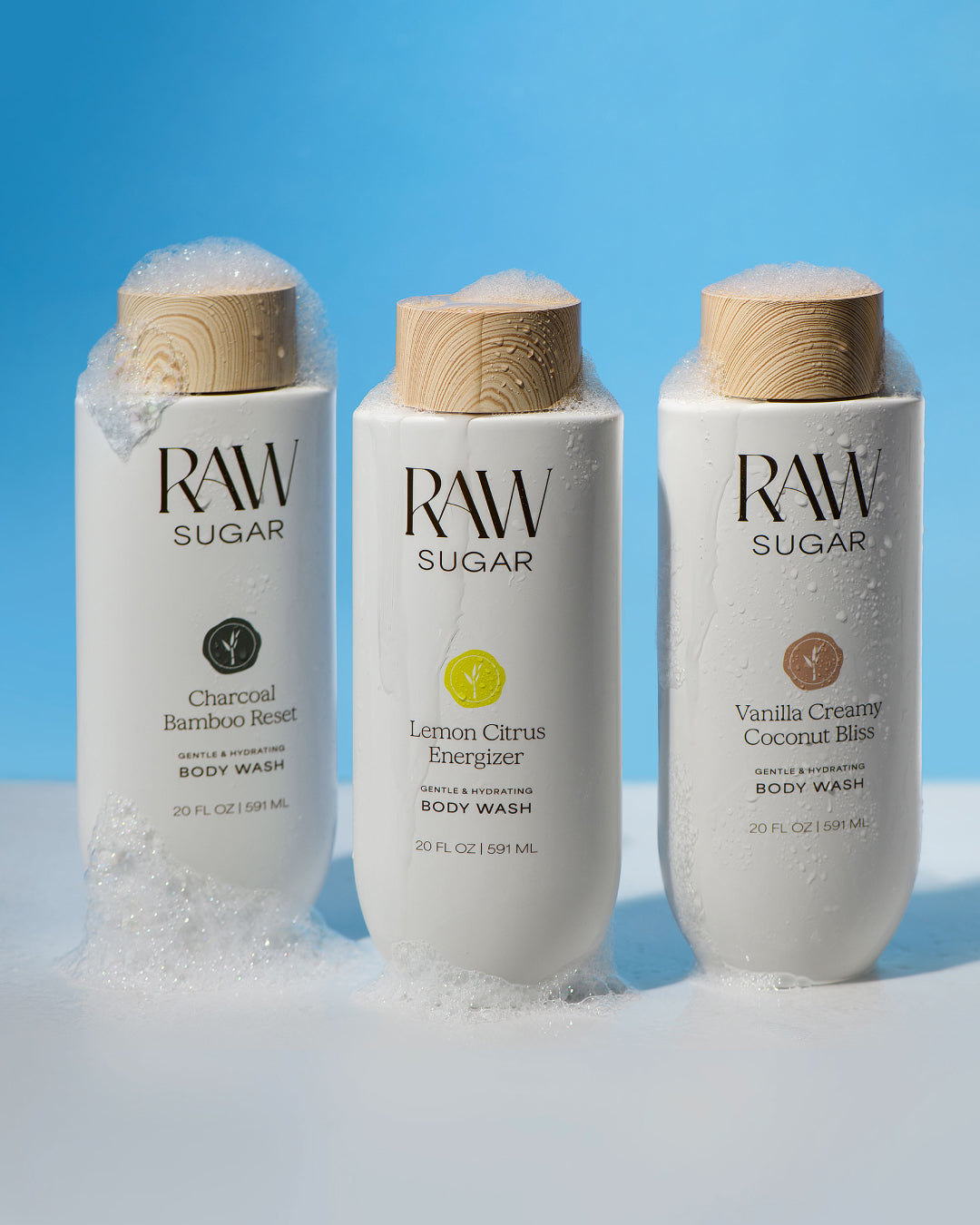 Three bottles of Raw Sugar body wash with wooden caps on a blue background