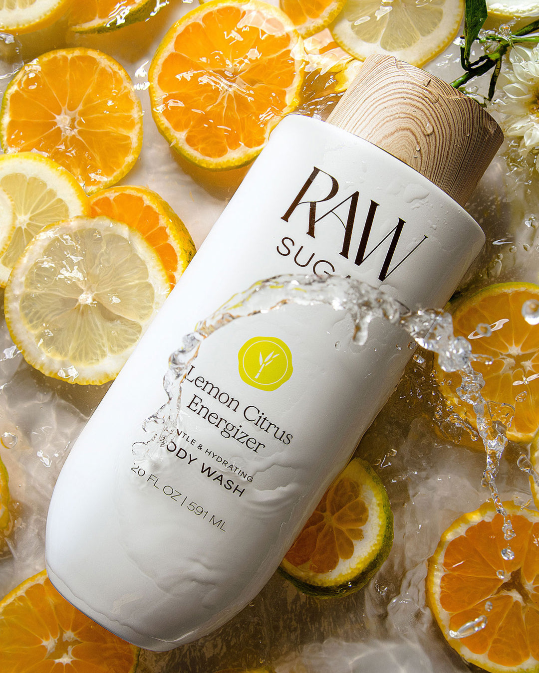 Body wash bottle labeled 'Raw Sugar' surrounded by sliced oranges and lemons on a wet surface.