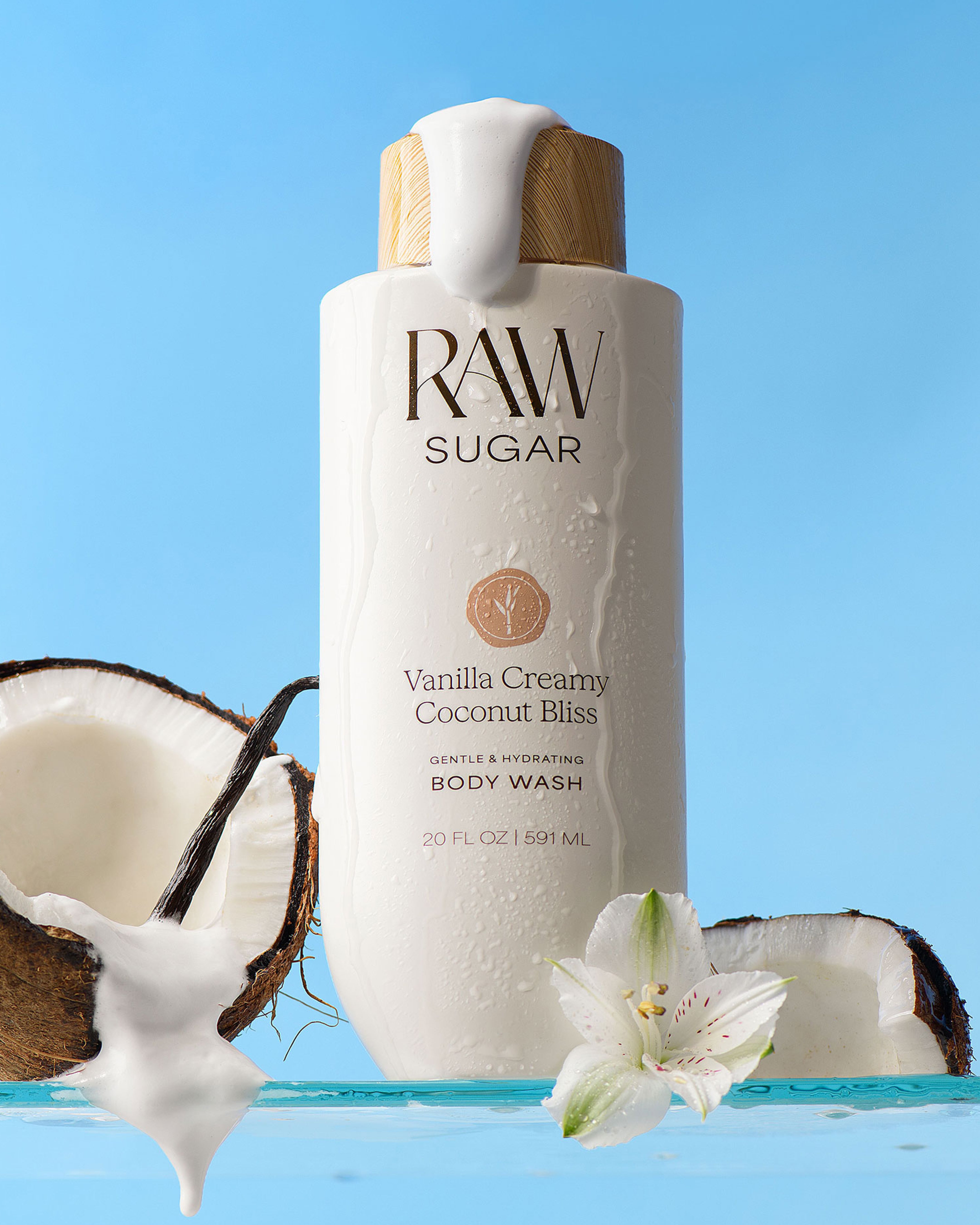 RAW Sugar Vanilla Creamy Coconut Bliss body wash bottle with coconut and flower on a blue background