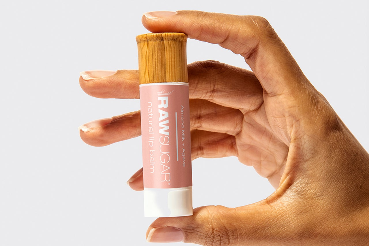 Hand holding a lip balm stick with a bamboo cap on a light gray background