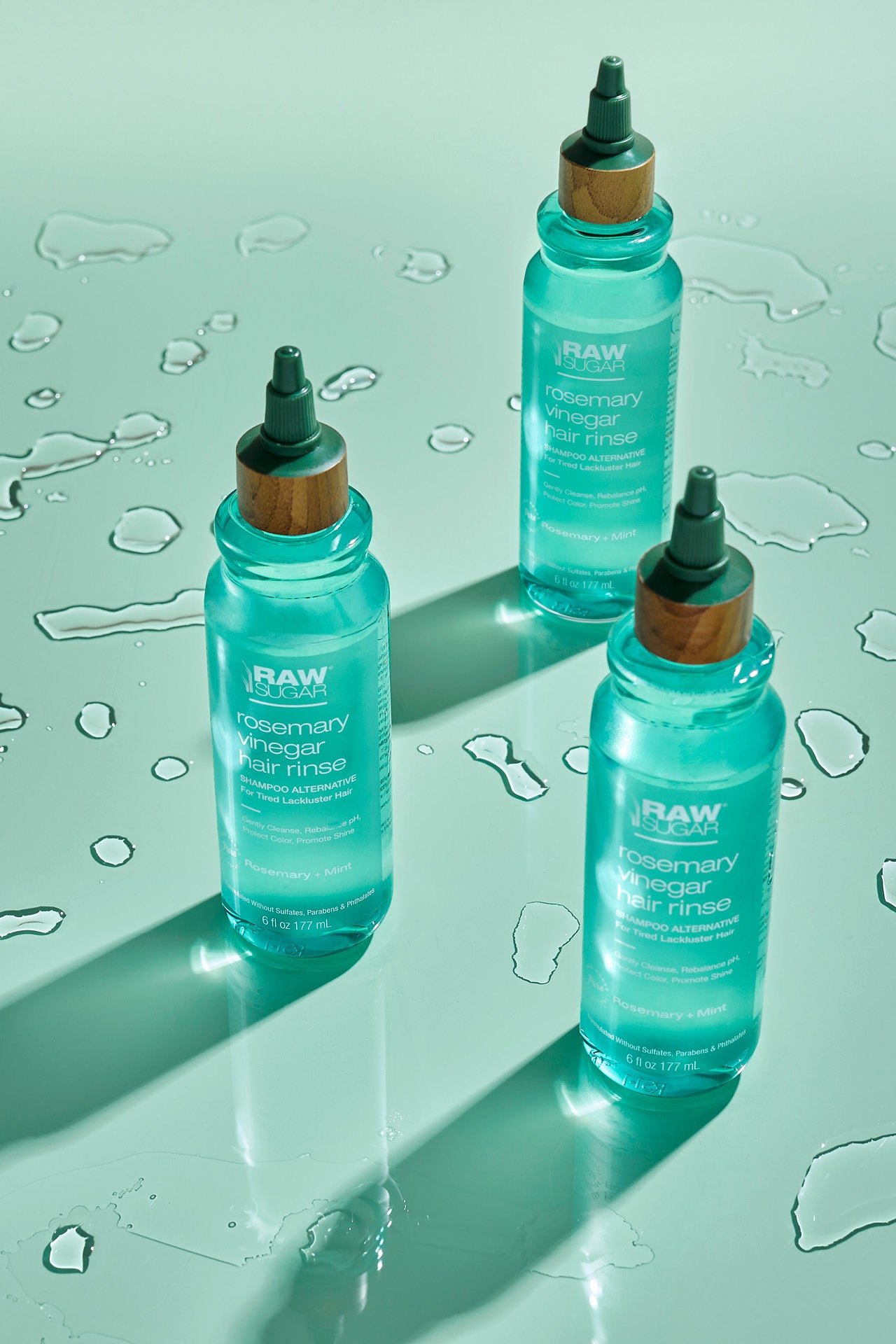 three bottles of rosemary vinegar rinse sitting on colored floor with water drops