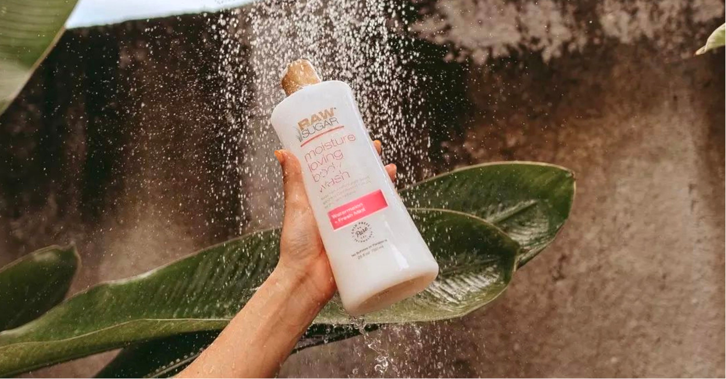 hand holding body wash in front of waterfall