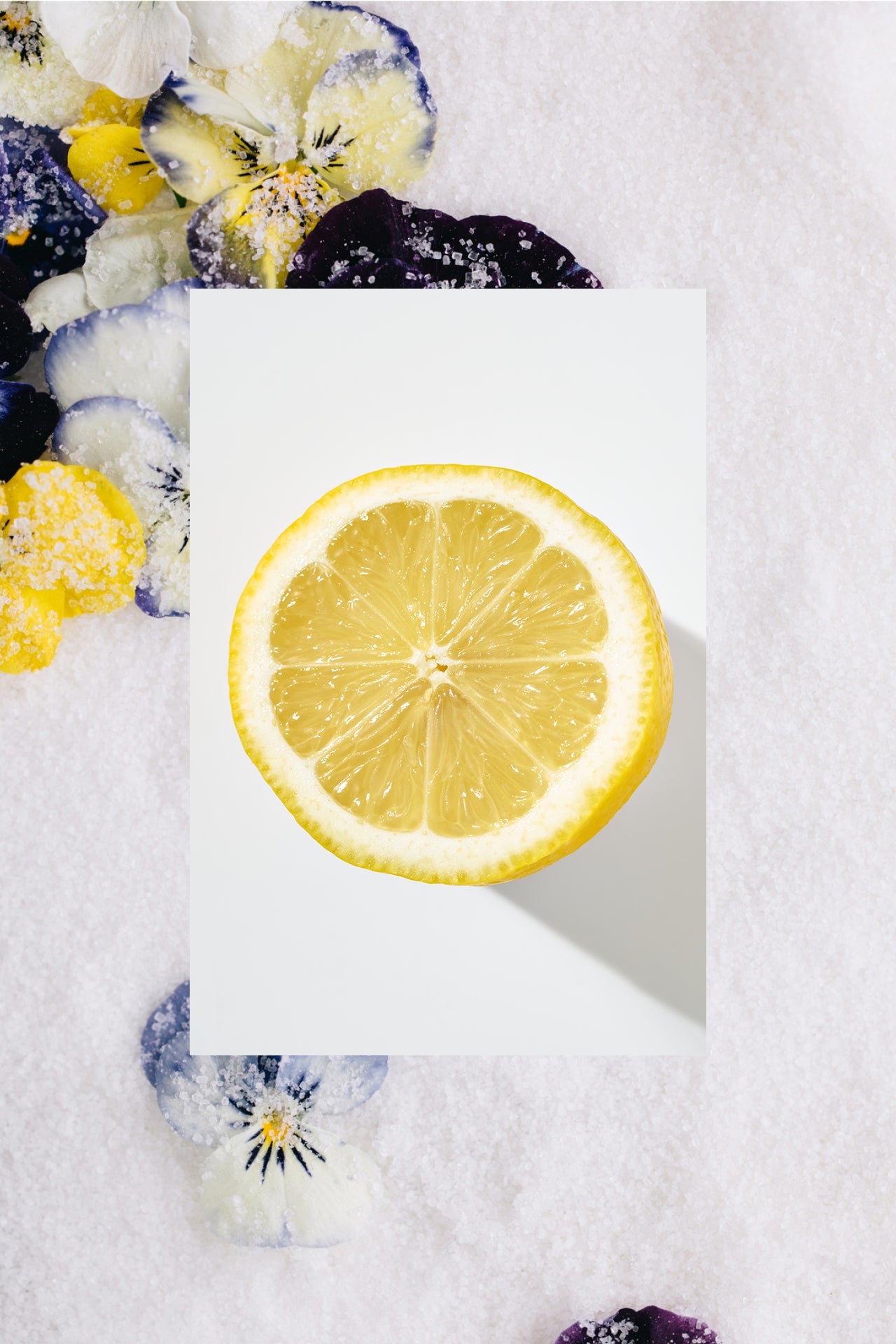 lemon half in front of sugar granules with flower petals