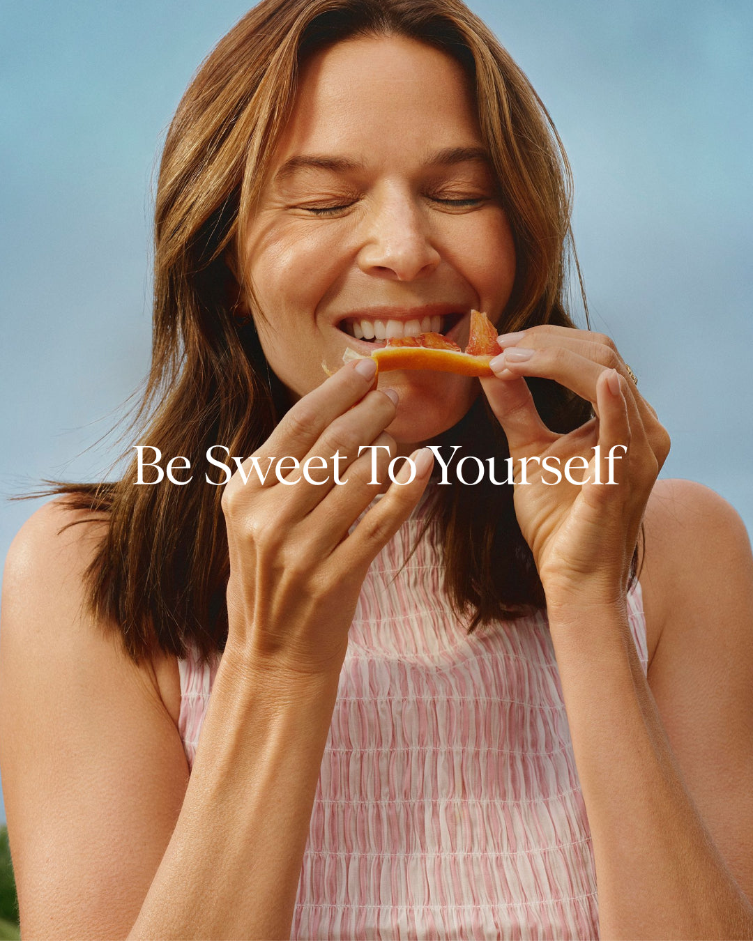 Woman eating an orange with 'Be Sweet To Yourself' text on a blue background