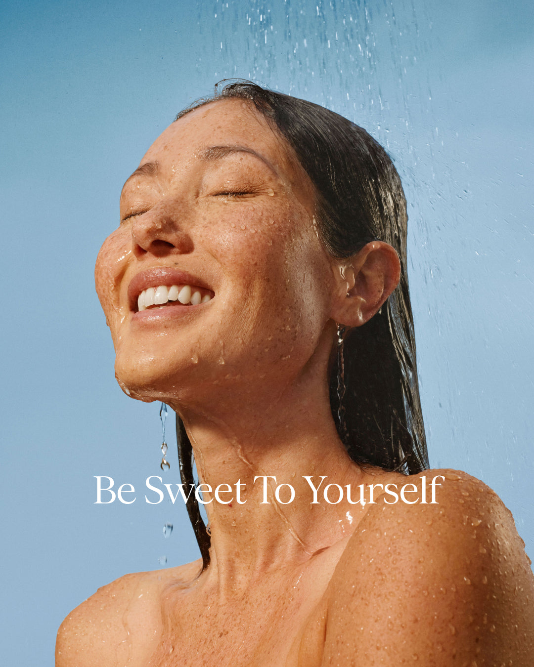 Woman under shower with 'Be Sweet To Yourself' text on a clear blue sky background