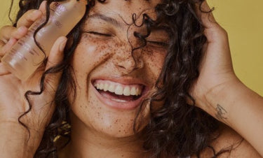 Women Smiling and Holding Hair Oil Next to Face