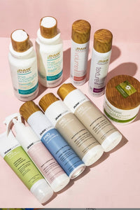 Various Pro Remedy Products Lying Flat Surrounded by Shampoo and hair masques on light pink background