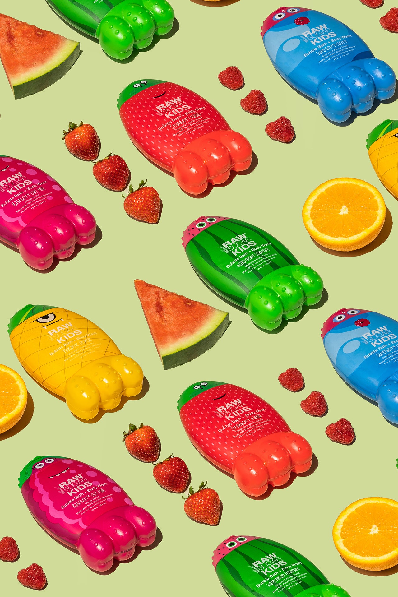 Rows of colorful Raw Sugar Kids bubble bath Monsters laying side by side alternating with fresh strawberries and watermelon slices