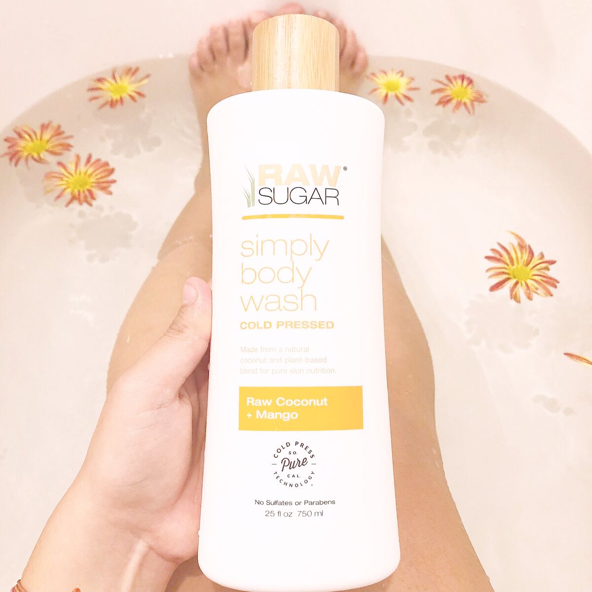 person in bathtub holding Lemon Sugar Body Wash with flowers floating in water