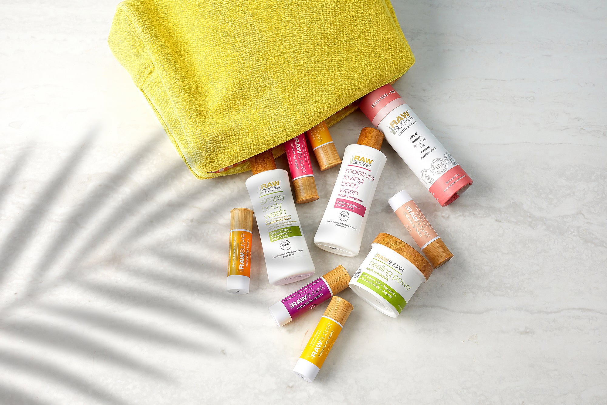 Raw Sugar travel sized products in a travel cosmetic bag and palm tree shadow