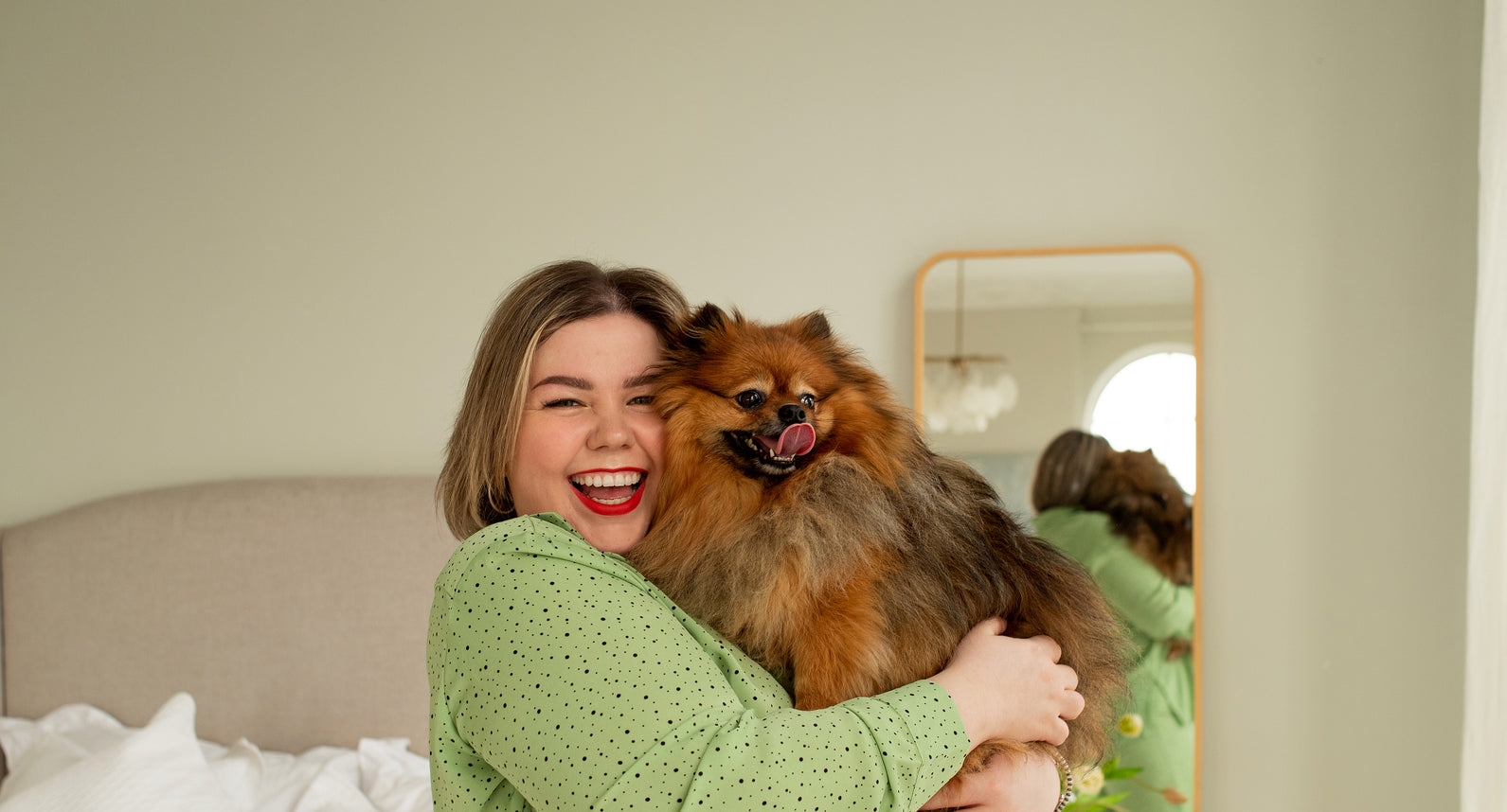 girl smiling and holding fluffy dog in bedroom
