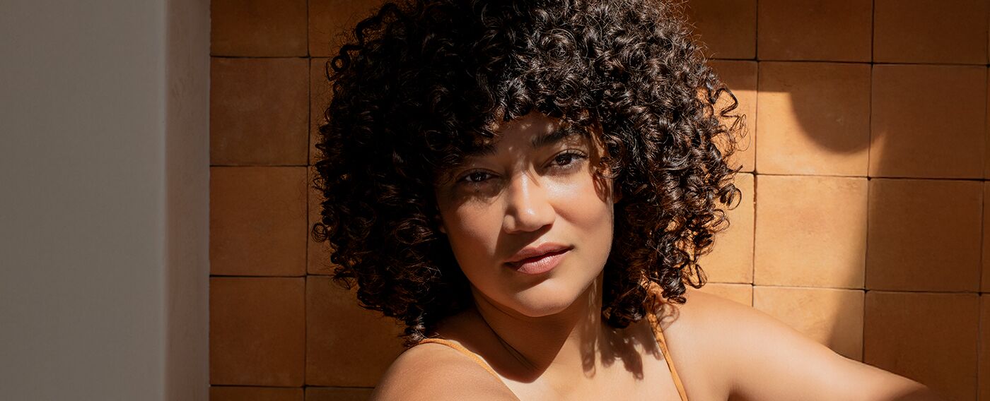girl with curly hair smiling in front of a tile bathroom
