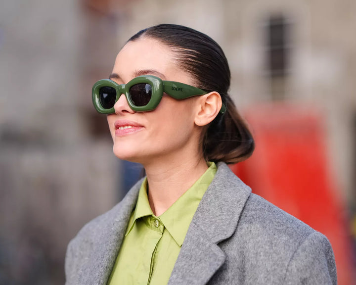 Woman with slick back tied hair and green sunglasses