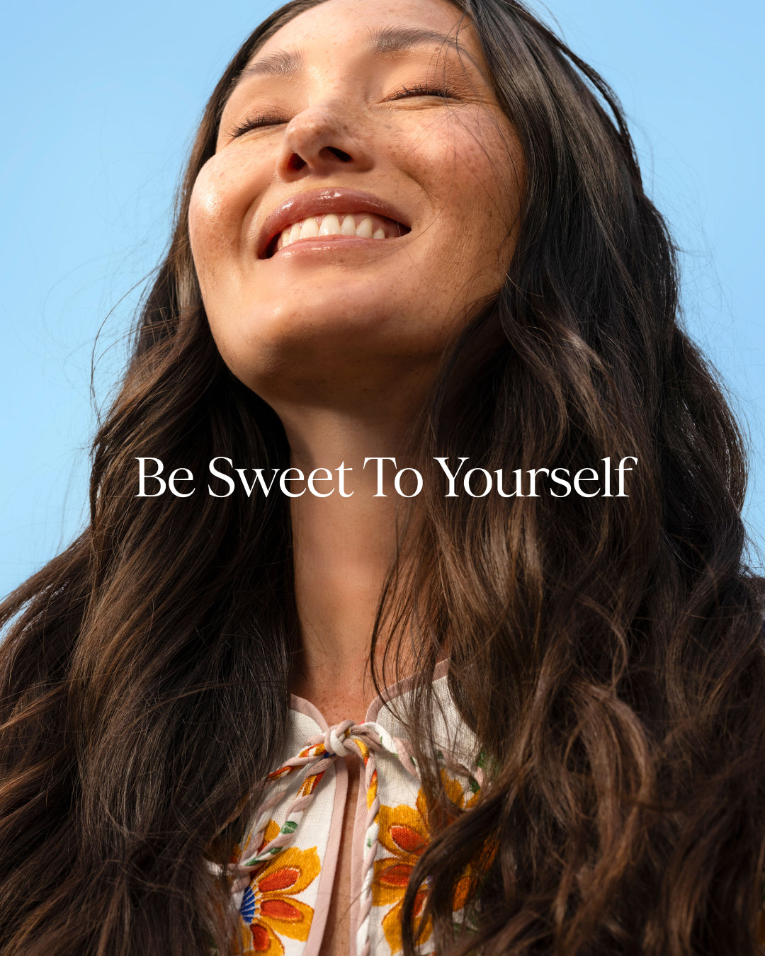 Woman with long dark hair against a clear blue sky with 'Be Sweet To Yourself' text.