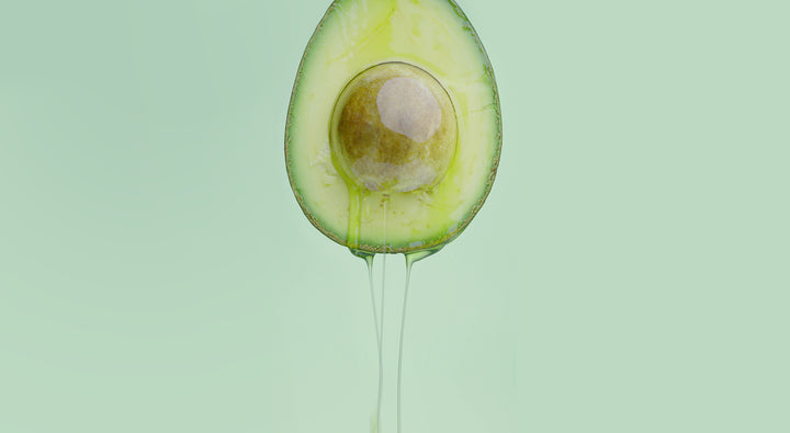 avocado dripping avocado oil in front of green background