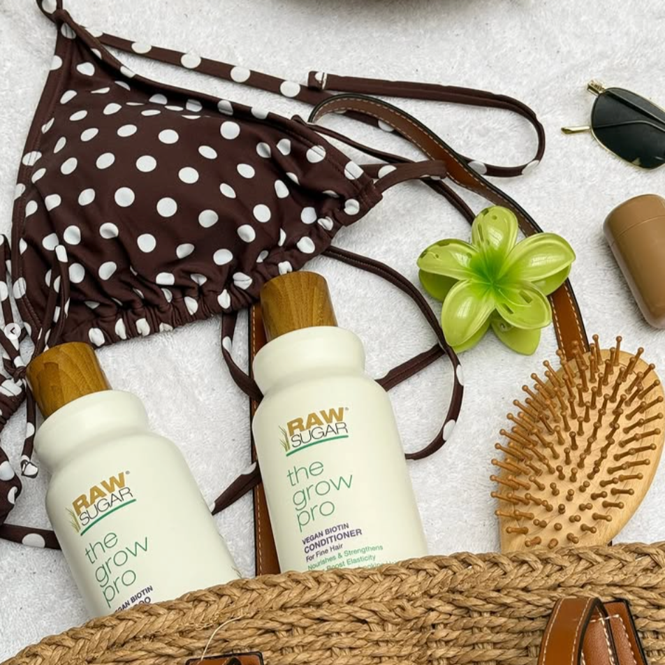 Two bottles of 'Raw & Clean' hair care products with a bikini, straw bag, and accessories on a light background.