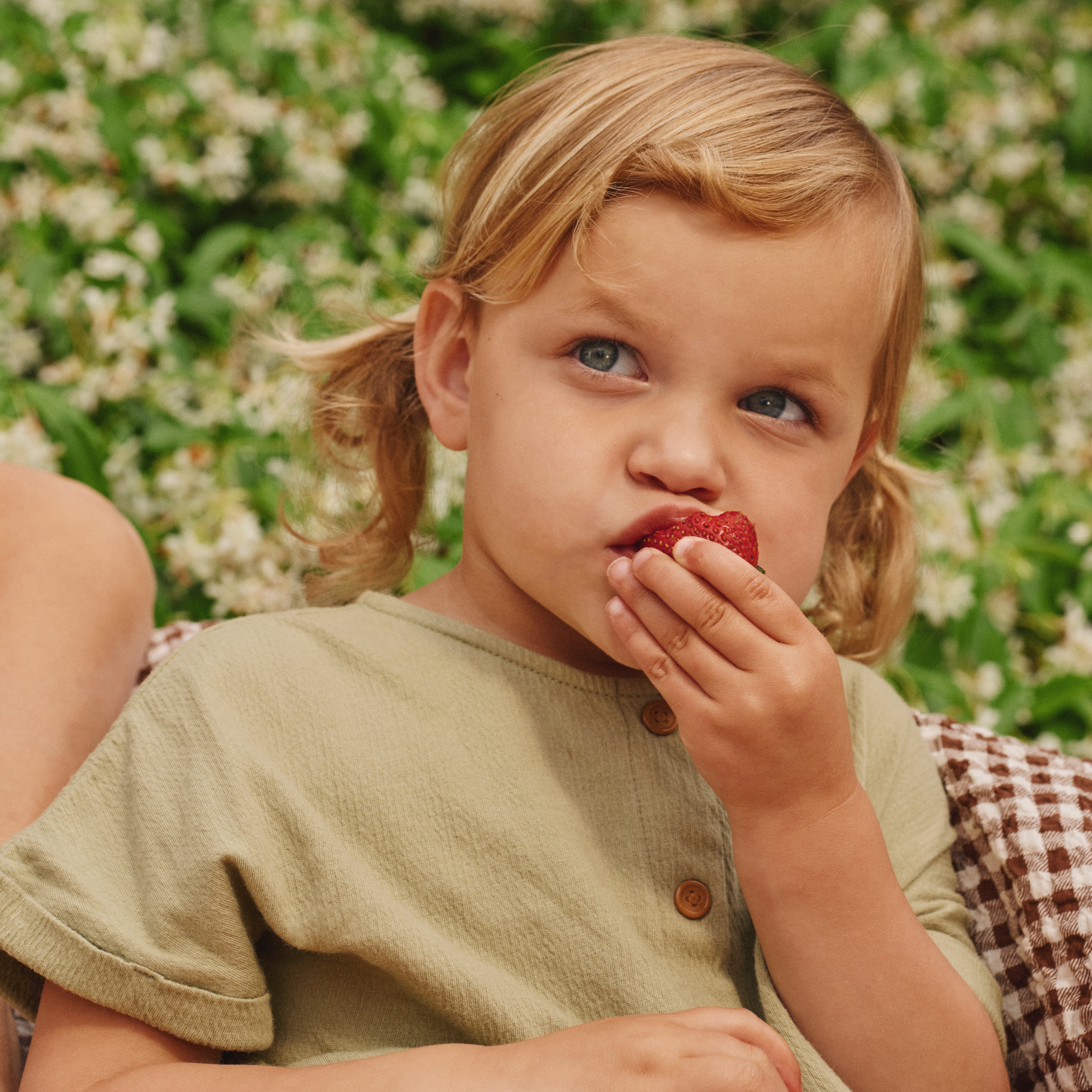 Child eating a strawberry outdoors with greenery in the background