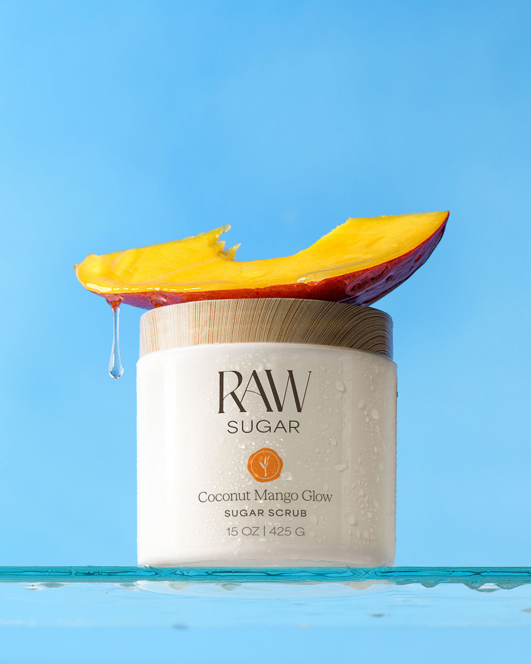 Jar of Raw Sugar Coconut Mango Glow sugar scrub with a mango slice on a blue background