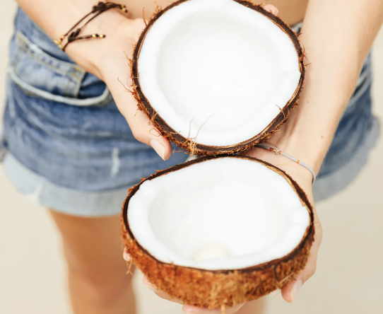 hands holding two coconut halves in front of jean shorts