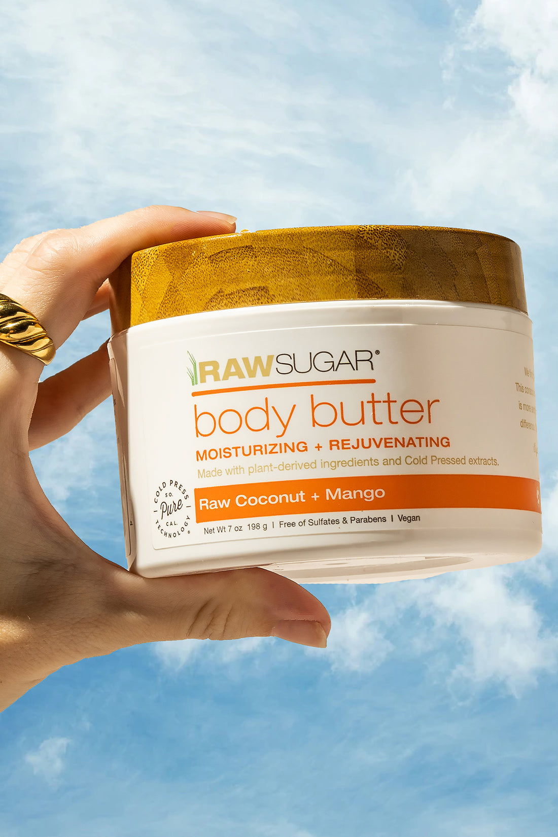 hand holding mango body butter against sky background