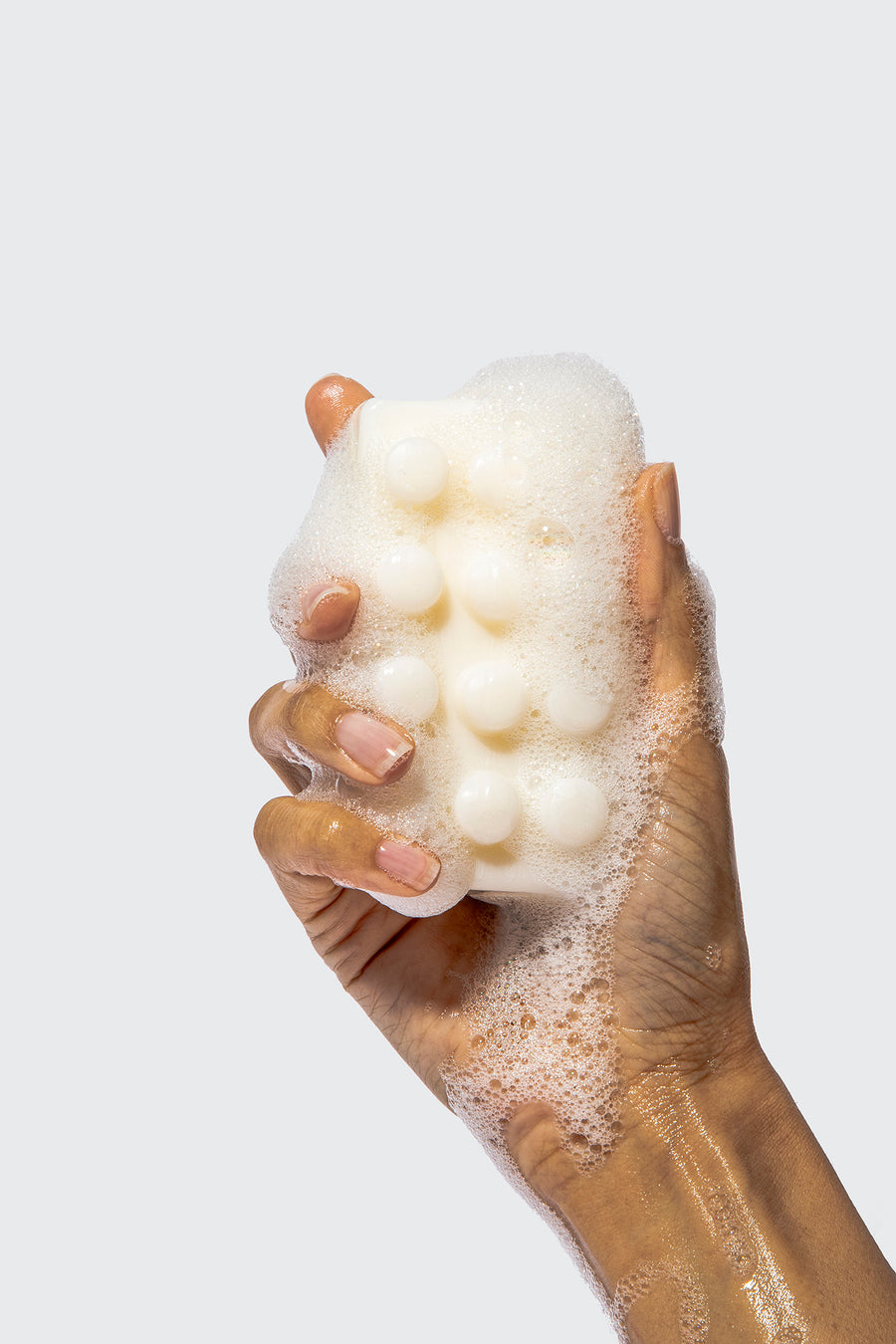 Hand holding bar of soap with white foamy suds dripping down