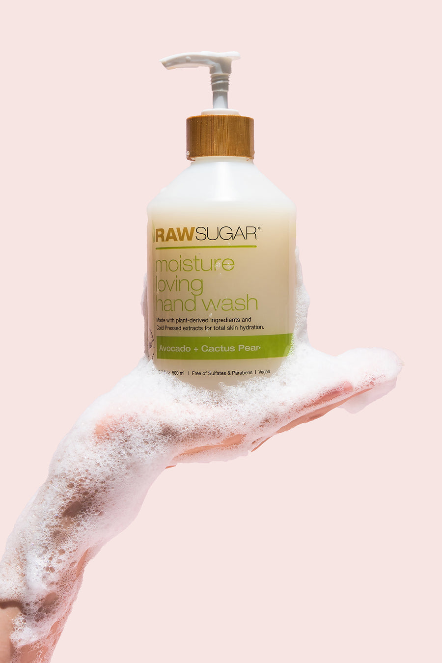 A sudsy and white lathered hand holding a Raw Sugar Moisture Loving Hand Wash bottle of Avocado + Cactus Pear 