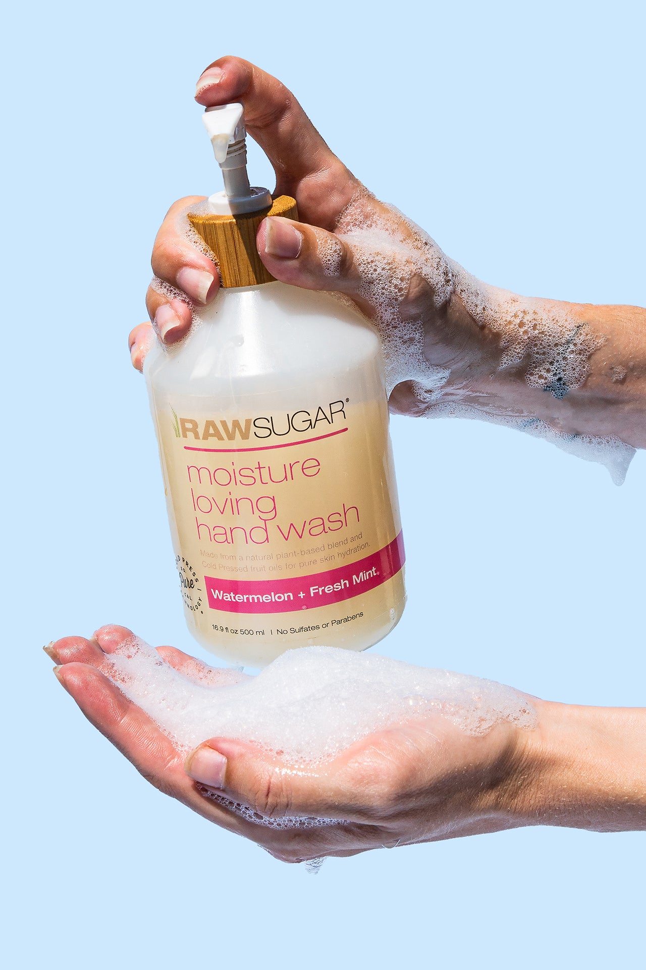 Lathered up sudsy hands holding Raw Sugar Moisture Loving Hand Wash Watermelon + Fresh bottle 