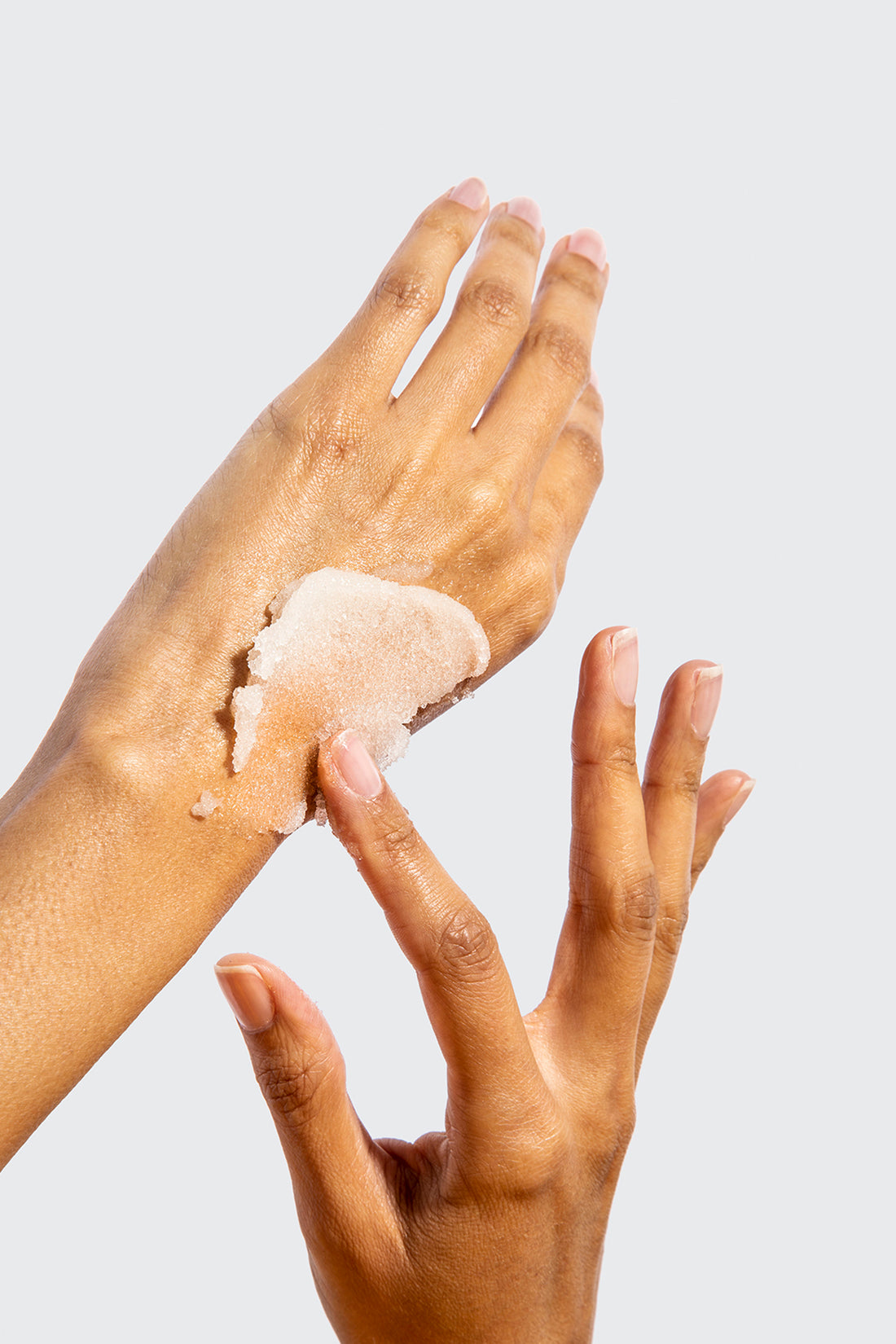 a pair of hands apply scrub to top of one hand