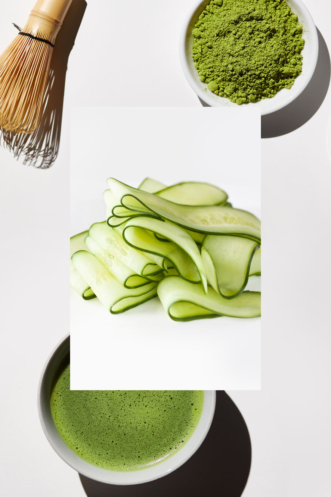 Bamboo tea whisk, bowl of matcha tea powder, cucumber slices and a bowl of liquid matcha tea.
