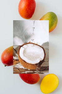 A raw coconut half with water dripping down to fill up half and fresh mangos
