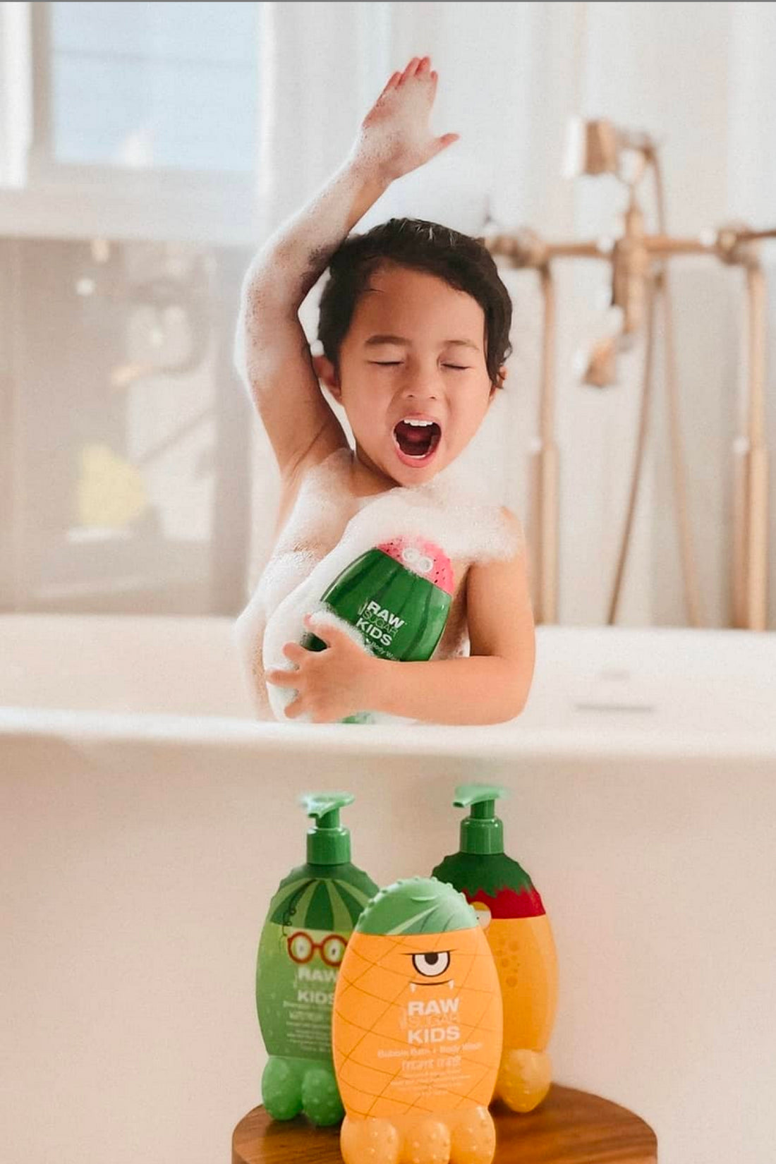 Kid Yawning in Tub and Reaching Hand Up Holding Body Wash with products in front