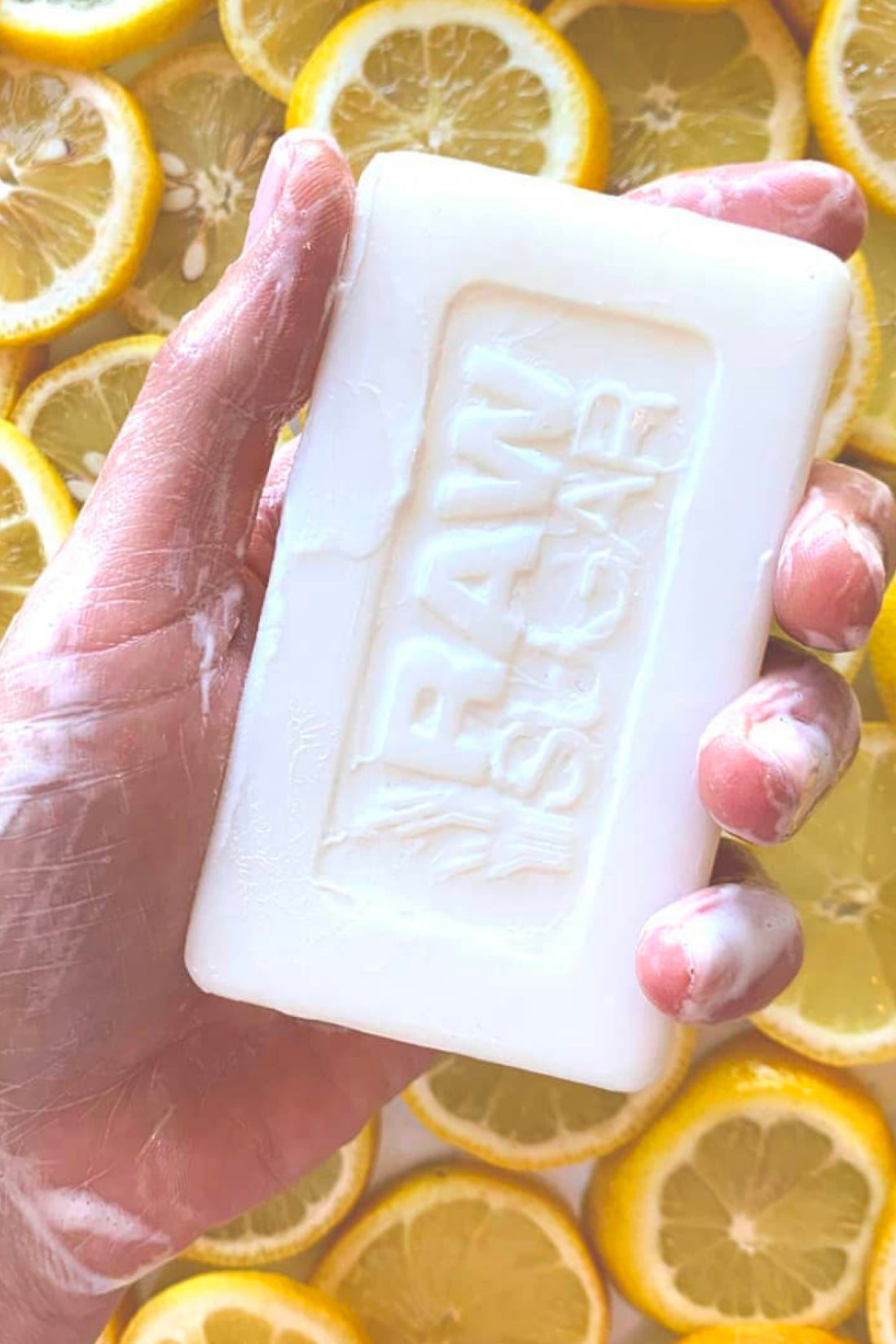 Hand Holding Bar Soap in front of Lemon Slices