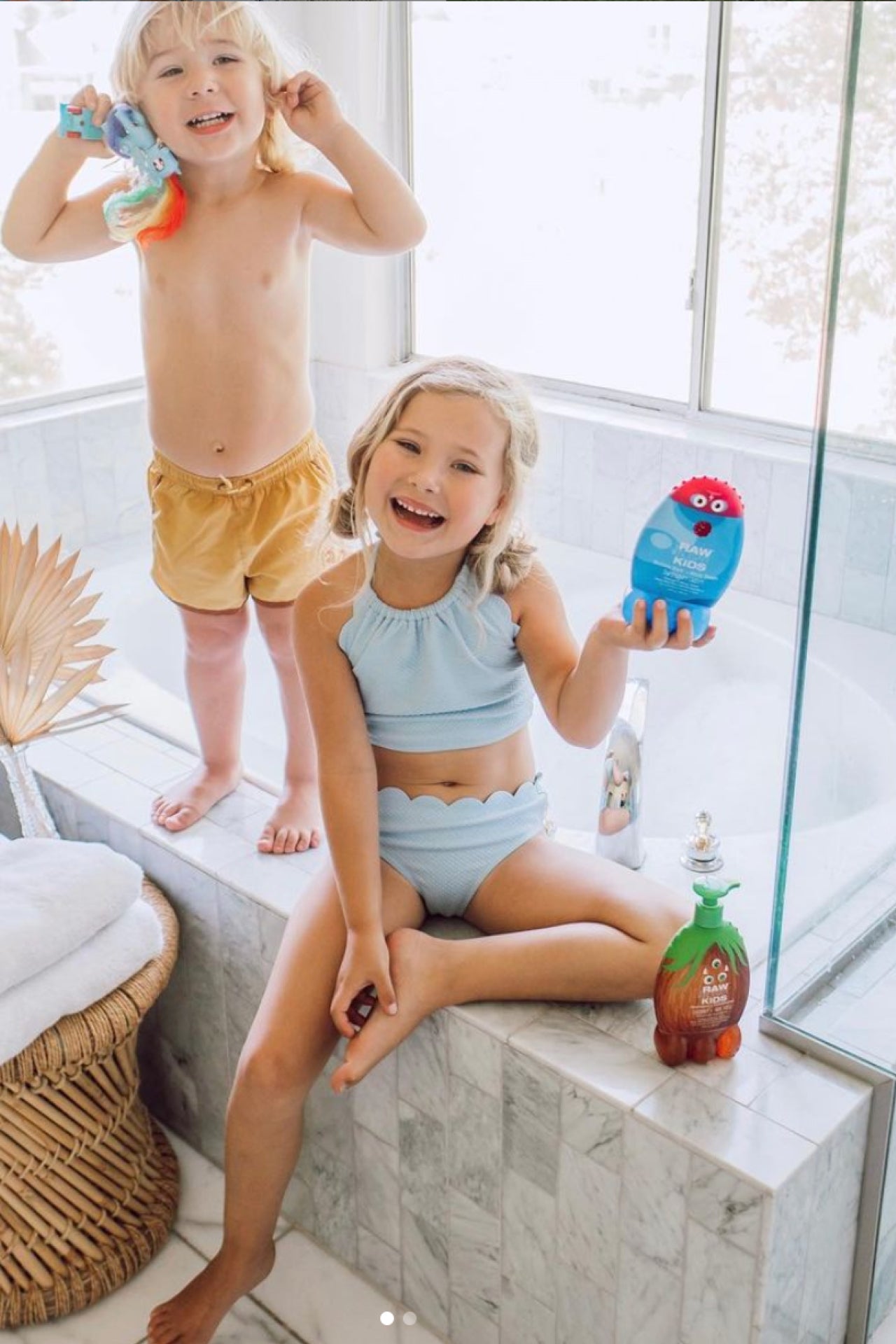 Two Kids in Bathing Suits playing near tub holding Kids Products