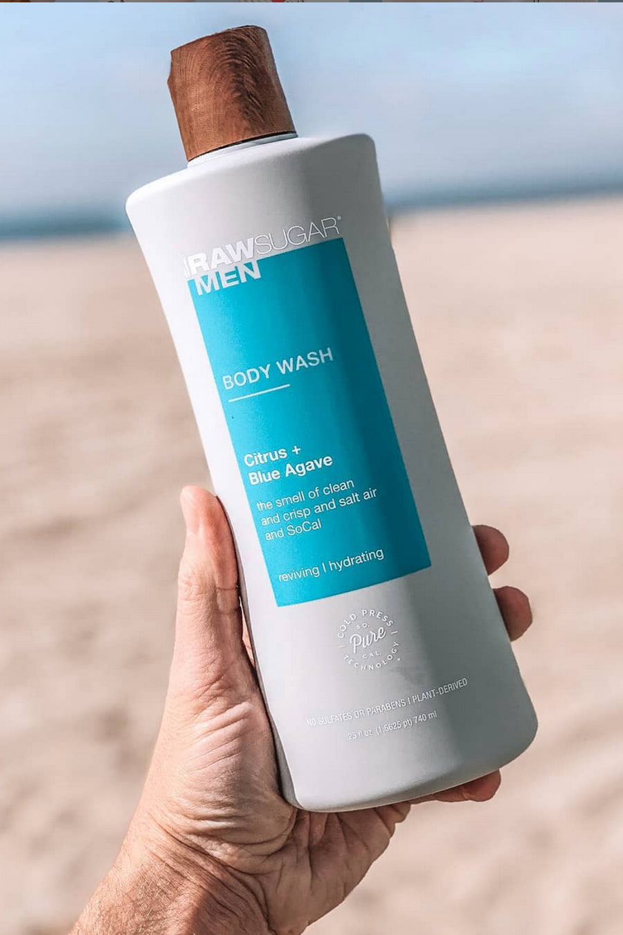 hand holding body wash in front of beach