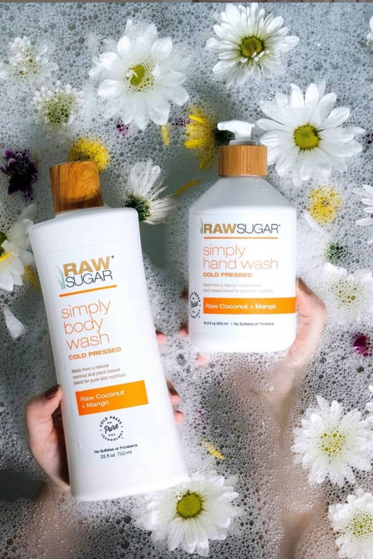 Raw Sugar Hand Wash and Body Wash laying in bath next to flowers and suds.
