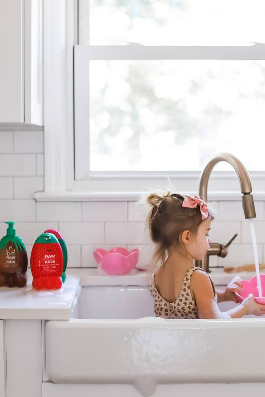 Girl playing in sink filling up a pink bowl with kids products to her left