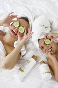 parent and child laying in bed in towels after back with Raw Sugar Body Wash and Lotion next to them holding cucumbers on their eyes