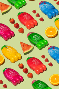  Rows of colorful Raw Sugar Kids bubble bath Monsters laying side by side alternating with fresh strawberries and watermelon slices