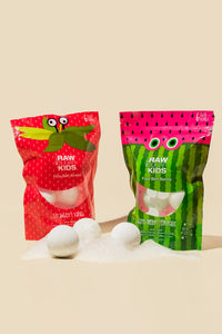 Two bags of both scents of Raw Sugar Kids Bath fiizzers with 3 fizzer balls in front bag on sugar