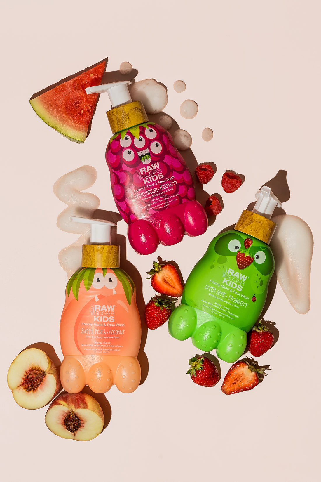 Raw Sugar Kids Monster Foamy Hand + Face Wash bottles lying amongst fresh peaches, strawberries , raspberries, and watermelon