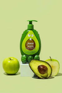 Kids Lotion with Avocado and Apples Next to It on Green Background