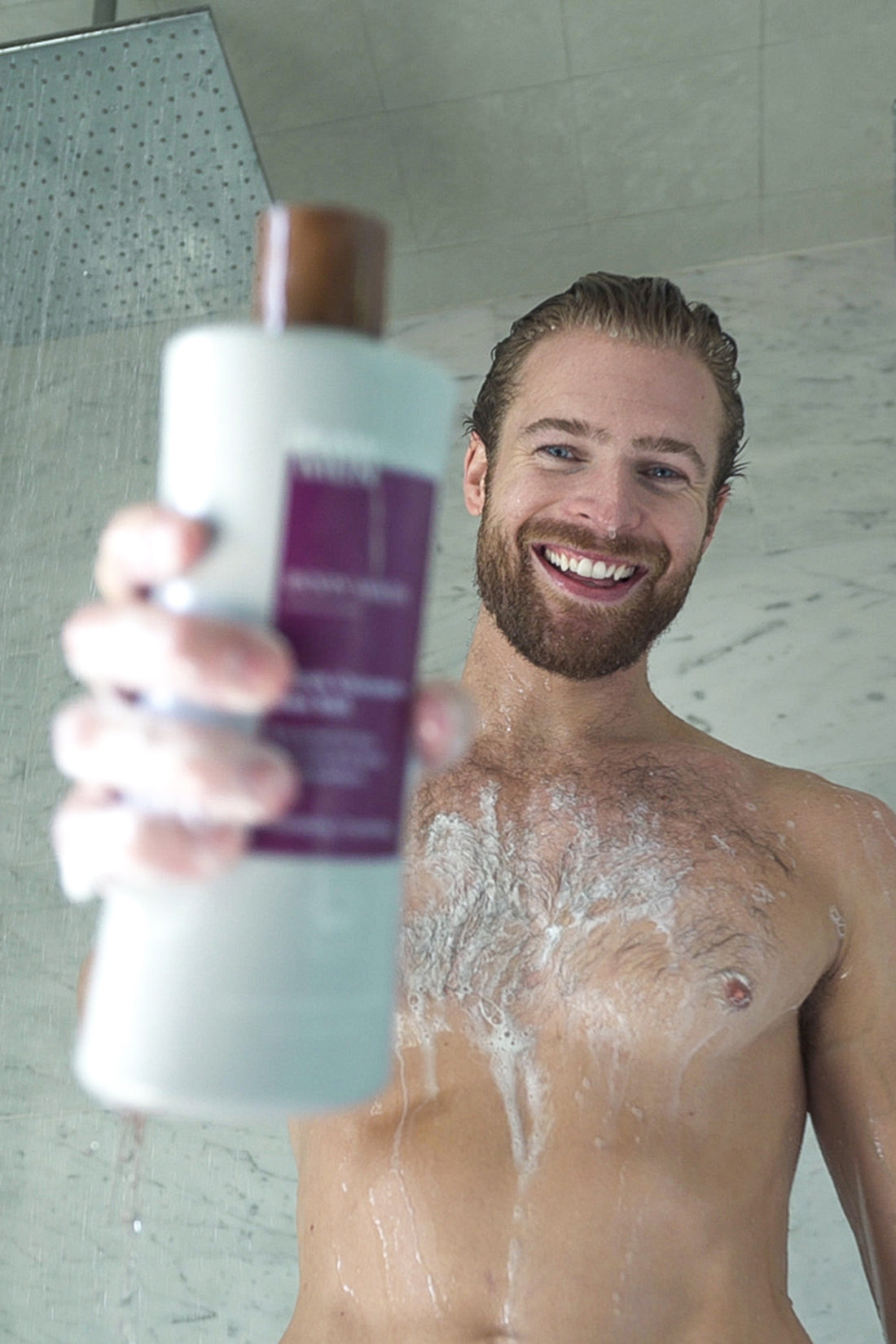 Smiling man in shower with white suds on his chest and fingers holding a Raw Sugar Body Wash bottle
